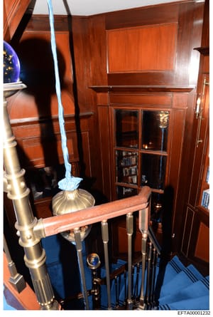 This photograph shows the interior of a yacht cabin featuring rich mahogany wood paneling, built-in shelving with glass doors, brass fixtures, and blue carpeting. The image captures upscale maritime furnishings and décor consistent with Epstein's kno