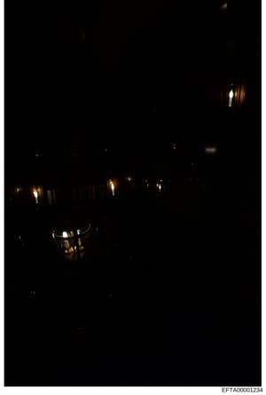 This is a nighttime photograph showing the exterior of a building with multiple illuminated windows visible against a dark facade. Several windows display warm interior lighting, suggesting occupied spaces. The image appears to be evidence documentat