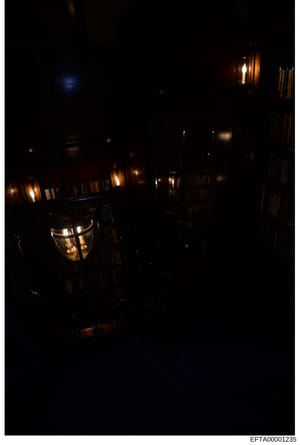 This is a nighttime photograph of an interior space, likely a hallway or corridor in a residential or commercial property. The image shows multiple wall-mounted light fixtures (sconces) illuminating the space with warm, golden lighting against dark w