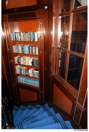 This photograph shows a built-in wooden bookcase with glass-fronted doors containing DVDs, Blu-rays, and books. The image appears to be an inventory or property documentation photo, likely taken during the investigation of an Epstein property. The bo