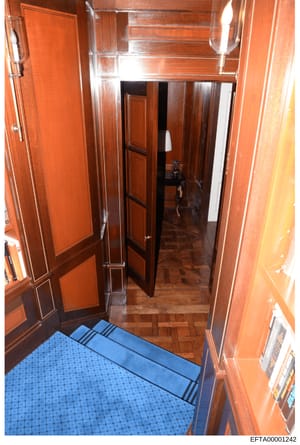 This photograph shows an interior entryway or hallway featuring rich reddish-brown wood paneling on walls and doors, a herringbone wood floor, and a blue entry mat. The image appears to be part of a property documentation or evidence collection, show