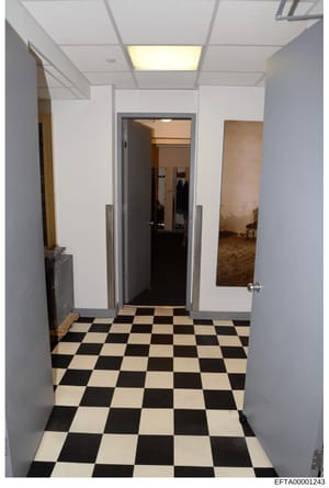 Photograph showing a hallway interior with distinctive black and white checkerboard tile flooring, white walls, recessed lighting, and multiple doorways. The image appears to be documentation of a residential or commercial interior space, possibly pa