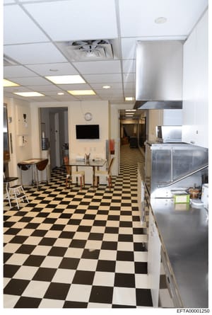 This is an evidence photograph documenting the interior of a kitchen and common area space, featuring a distinctive black and white checkered floor pattern, stainless steel appliances, drop ceiling with recessed lighting, and a mounted television. Th