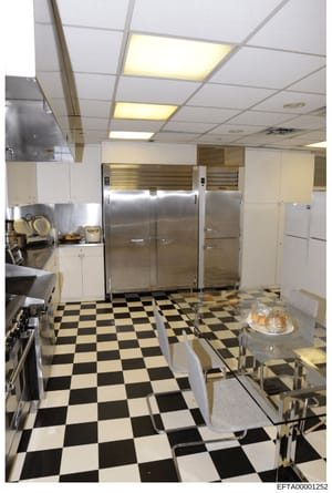 This is a photograph of a large commercial or institutional kitchen, showing professional-grade stainless steel refrigeration units, commercial cooking equipment, and a distinctive black-and-white checkered floor. The image appears to be documentatio