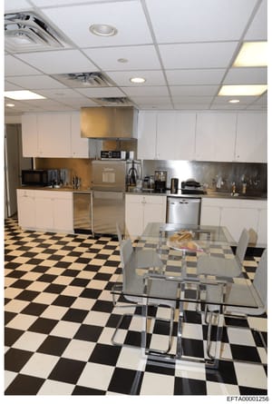 This photograph documents the interior kitchen of an Epstein property, showing a modern kitchen with white cabinetry, stainless steel appliances, a metal dining table with chairs, and a distinctive black-and-white checkered floor. The image appears t