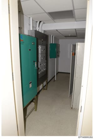 This photograph shows an interior utility room containing electrical infrastructure, including turquoise-colored power distribution panels, electrical boxes, and related equipment. The image appears to be documentation of building systems, possibly t
