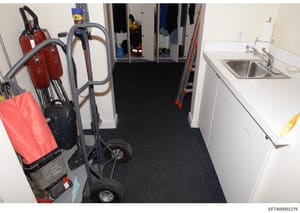 This is an evidence photograph of a utility or service room, likely from one of Jeffrey Epstein's properties. The image shows cleaning and maintenance equipment including fire extinguishers, commercial carpet cleaning machines, storage closets, and a