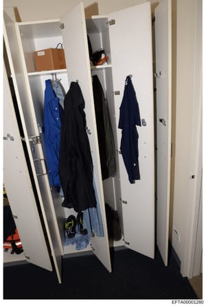 This is a photograph of a built-in closet containing various clothing items including jackets, coats, and other garments in blue, black, and denim colors, along with a brown bag and miscellaneous items on shelves. The photo appears to be evidence doc