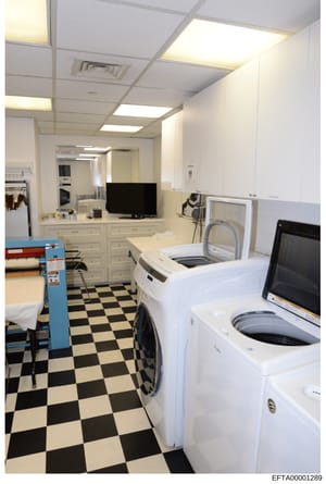 This photograph documents the interior of a laundry and utility room, showing multiple washing machines, dryers, cabinetry, and monitoring equipment. The image appears to be evidence documentation from a property investigation, capturing the operatio