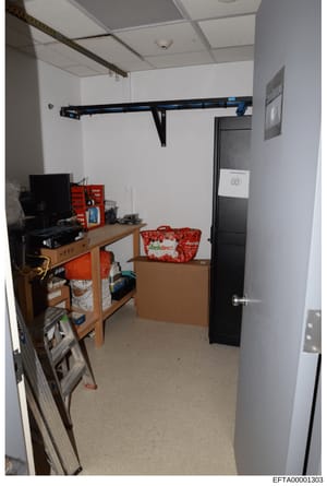 This is an evidence photograph showing an interior room or storage space, likely from a property inspection during the investigation. The room contains a wooden desk with computer equipment, red storage containers marked 'freshdirect', metal shelving