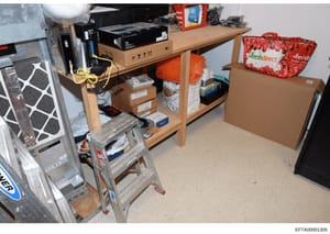 This is an evidence photograph showing the interior of a storage room or garage space containing various household items, electronics, and supplies. The image documents the physical contents and layout of what appears to be a residential storage area