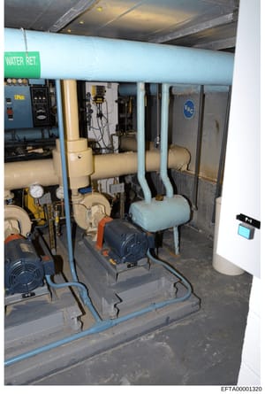 This is a photograph of an interior mechanical room showing a water retention and circulation system. The image shows various pipes, pumps, tanks, control panels, and electrical equipment. The green label reading 'WATER RET.' is visible on the main b