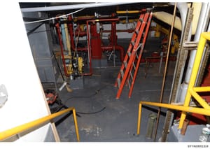 This photograph shows an interior mechanical or engine room with industrial fire suppression systems, HVAC equipment, and various piping infrastructure. The image captures red and yellow safety equipment, including what appears to be fire suppression