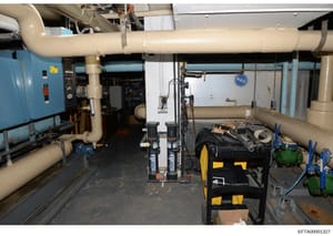 This photograph documents an industrial or commercial mechanical/utility room, likely from one of Epstein's properties. The image shows extensive HVAC ductwork, plumbing infrastructure, pumps, and mechanical equipment in what appears to be a basement