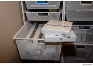 This photograph documents computer equipment and peripheral devices, including Apple brand items and a USB SuperDrive, stored in white mesh organizational containers. The image appears to be evidence documentation from a property seizure, with items 