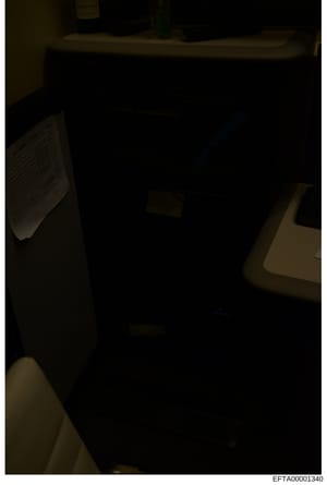 This is a poorly lit photograph of an interior room, likely taken during an evidence-gathering investigation. The image shows minimal detail due to low lighting conditions, with only shadowy outlines of furniture and fixtures visible. The photograph 