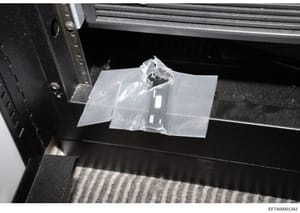 This is a photograph of a small item sealed in a clear plastic evidence bag, positioned on what appears to be a black evidence collection table or surface. The item's specific nature is obscured by the packaging and angle of the photograph. The image