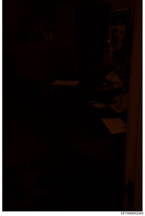 This is a poorly lit photograph of an interior room, likely from a property associated with the investigation. The image is extremely dark with minimal visibility, showing what appears to be wooden furniture or fixtures. The quality and darkness make