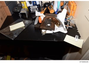 This is an evidence photograph showing various seized items laid out on a black table for documentation purposes. The collection includes electrical equipment, grooming tools (WAHL brand clippers and trimmers), wooden boxes or panels, cardboard boxes