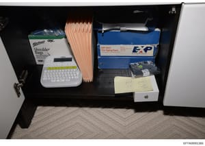 This photograph documents the contents of a desk drawer or office space, showing various items including office supplies, electronics, and paperwork. The image appears to be evidence documentation from the investigation, captured with a clear view of