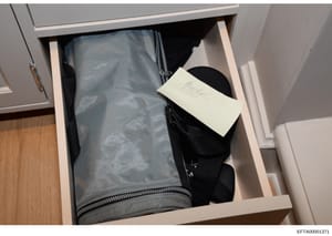 This is a forensic evidence photograph showing items recovered during a search, documented in a white drawer. The photo includes a gray mesh bag with zipper closure and a black item, with a handwritten evidence label attached. This type of photo serv