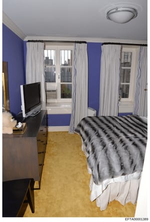 This is an evidence photograph documenting an interior bedroom space, likely from one of Epstein's properties. The image shows a modernly decorated room with distinctive blue walls, multiple windows with white curtains offering city views, a bed with