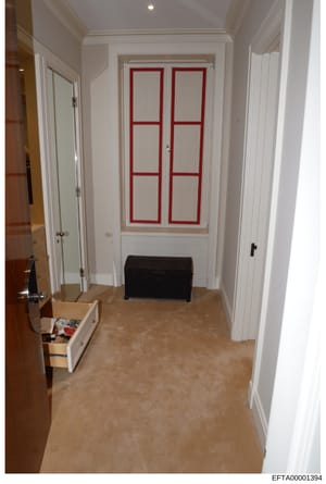 This photograph depicts an interior hallway of what appears to be a residential property, showing white painted walls, cream-colored flooring, multiple white doors on either side, and a distinctive pair of French doors with red frames in the center b