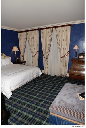 This is a photograph of a furnished bedroom, likely taken during a property inspection or inventory documentation. The room features coordinated blue wall treatment, cream-colored patterned curtains, wooden furniture including nightstands and a dress