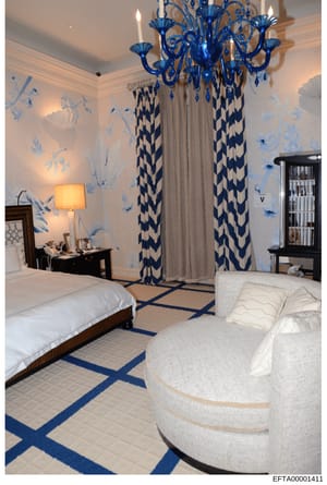 This is a photograph of an upscale residential bedroom featuring coordinated blue and white interior design. The room displays high-end furnishings including a ornate blue Murano-style chandelier, custom drapery with geometric patterns, antique furni