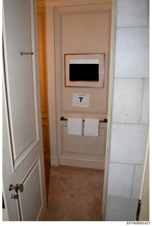 This photograph documents an interior bathroom space, likely from one of Jeffrey Epstein's properties seized during the investigation. The image shows a small bathroom with peach/salmon-colored walls, white trim, towel rack with white towels, and a f