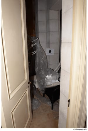 This is an evidence photograph from an investigation showing a bathroom interior with plastic-covered items and an evidence marker labeled 'R'. The photo documents the condition and contents of the space as part of the investigative process, with ite