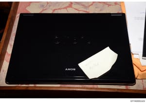 This is an evidence photograph showing a black Sony VAIO laptop computer positioned on a pink and white patterned surface. A white label with handwritten text reading '9405 Maddie' is affixed to the laptop's lid. The photo appears to be part of the i