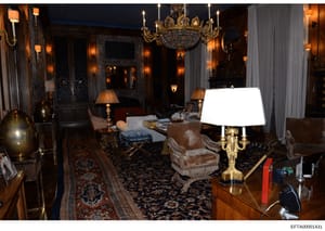 This is a photograph documenting the interior of one of Jeffrey Epstein's residences, showing an ornately decorated formal living room. The room displays luxury furnishings, including crystal chandeliers, fine upholstered seating, decorative lamps, a