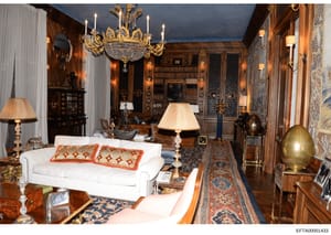 This photograph shows an elegantly appointed living room in a high-end residence, featuring formal décor with a grand chandelier, fine artwork, antique furniture, and refined architectural details. The space appears to be part of a substantial privat
