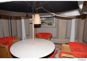 This is an evidence photograph showing an interior space with distinctive tent-like architecture, featuring a large white round table, red cushioned seating with wicker armrests, white cylindrical support columns, and cream-colored patterned fabric p