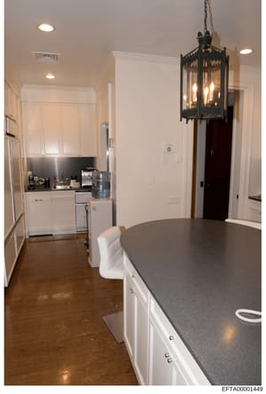 This is a photograph of a luxury kitchen and dining space showing high-end finishes and décor. The image depicts a modern kitchen with white cabinetry, black countertops, stainless steel appliances, recessed lighting, and a decorative black pendant f