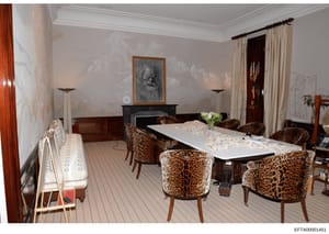 This photograph shows an elegantly furnished interior room, likely part of a residential or office property associated with the Epstein investigation. The room features a long white conference table surrounded by leopard-print upholstered chairs, cla