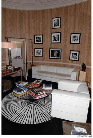This is an evidence photograph depicting the interior of a residential room, likely from one of Jeffrey Epstein's properties. The room features wood-paneled walls with multiple framed black-and-white photographs, contemporary furniture including whit