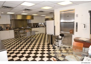 This photograph shows a large, professionally-appointed kitchen with commercial-grade appliances, likely from an Epstein property. The space features stainless steel equipment, white cabinetry, a black-and-white checkered tile floor, and an elevator 