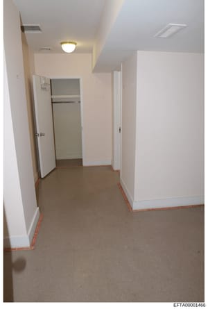 This is a photograph of an interior hallway with white walls, recessed lighting, and an open closet door revealing shelving. The hallway appears to be part of a residential property under investigation, with red tape marking visible on the floor bord