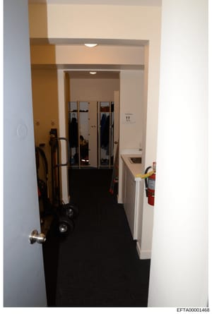This is a photograph of an interior hallway or corridor, showing built-in mirrored wardrobe doors, utility equipment including a hand truck and fire extinguisher, and basic facility furnishings. The image appears to be evidence documentation from a p