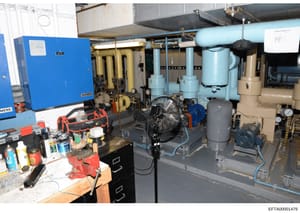This is a photograph of an industrial or commercial mechanical room showing HVAC equipment, piping systems, compressors, and related machinery. The image appears to be evidence documentation from a property inspection, showing the mechanical infrastr