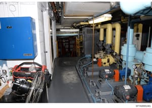 This photograph shows an industrial or commercial mechanical room containing HVAC equipment, pumps, pipes, electrical systems, and various tools. The image documents building infrastructure including a Siemens blue electrical panel, yellow piping sys