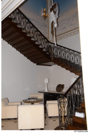 This is a photograph of an ornate interior space featuring a sweeping wooden staircase with decorative iron railings, classical ceiling details, and luxury furnishings. The image shows the architectural design and décor of what appears to be a high-e