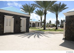 This is a color photograph showing the exterior grounds of a luxury property, likely one of Jeffrey Epstein's residences. The image depicts a spacious courtyard with pale stone flooring, black stone structures with white doors on either side, mature 