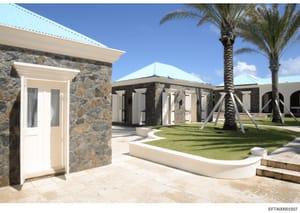 This photograph shows the exterior of a substantial residential property featuring modern stone construction with turquoise metal roofing, manicured lawns, and tropical landscaping. The image appears to be architectural documentation of an Epstein-li