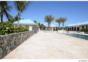 This photograph depicts an expansive tropical estate compound featuring stone architecture, a swimming pool, manicured grounds with palm trees, and distinctive turquoise-colored roof structures. The image appears to be evidence documentation of a pro