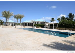 This is a photograph of a large luxury residential property featuring a swimming pool, extensive grounds with palm trees, and distinctive turquoise-roofed architecture. The image appears to be evidence documentation of a property owned or used by par