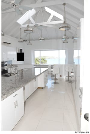 This photograph depicts a high-end modern kitchen featuring vaulted ceilings, multiple pendant lights, granite countertops, stainless steel appliances, and expansive ocean views through large windows. The image appears to be documentation of property