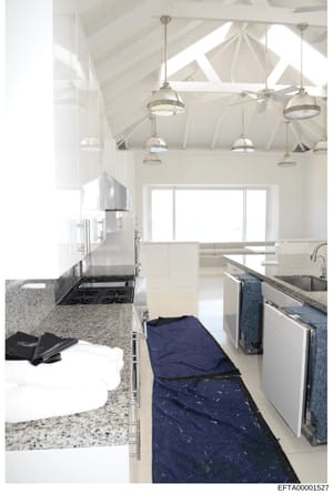 This is an interior photograph of a contemporary kitchen space featuring high vaulted ceilings with exposed white beams, multiple pendant light fixtures, granite countertops, stainless steel appliances, and a blue runner rug. The image appears to be 